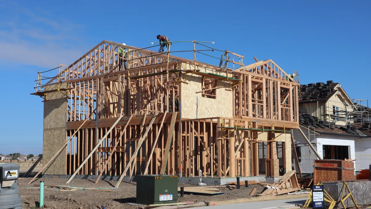 Two-story house framing under construction with roof work